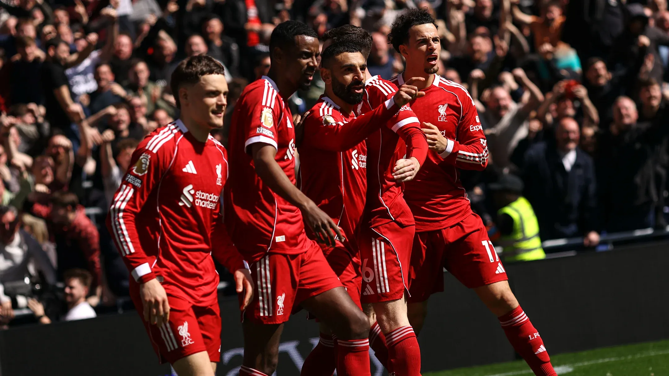 بازیکنان تیم لیورپول با لباس&zwnj;های قرمز یک&zwnj;دست، در حال جشن گرفتن گل در کنار زمین فوتبال هستند. رایان گراونبرخ با لبخند در جلو دیده می&zwnj;شود، در حالی که هاروی الیوت و محمد صلاح در کنار او و سایر هم&zwnj;تیمی&zwnj;ها در حال شادی و اشاره به تماشاگران پرشور در پس&zwnj;زمینه هست